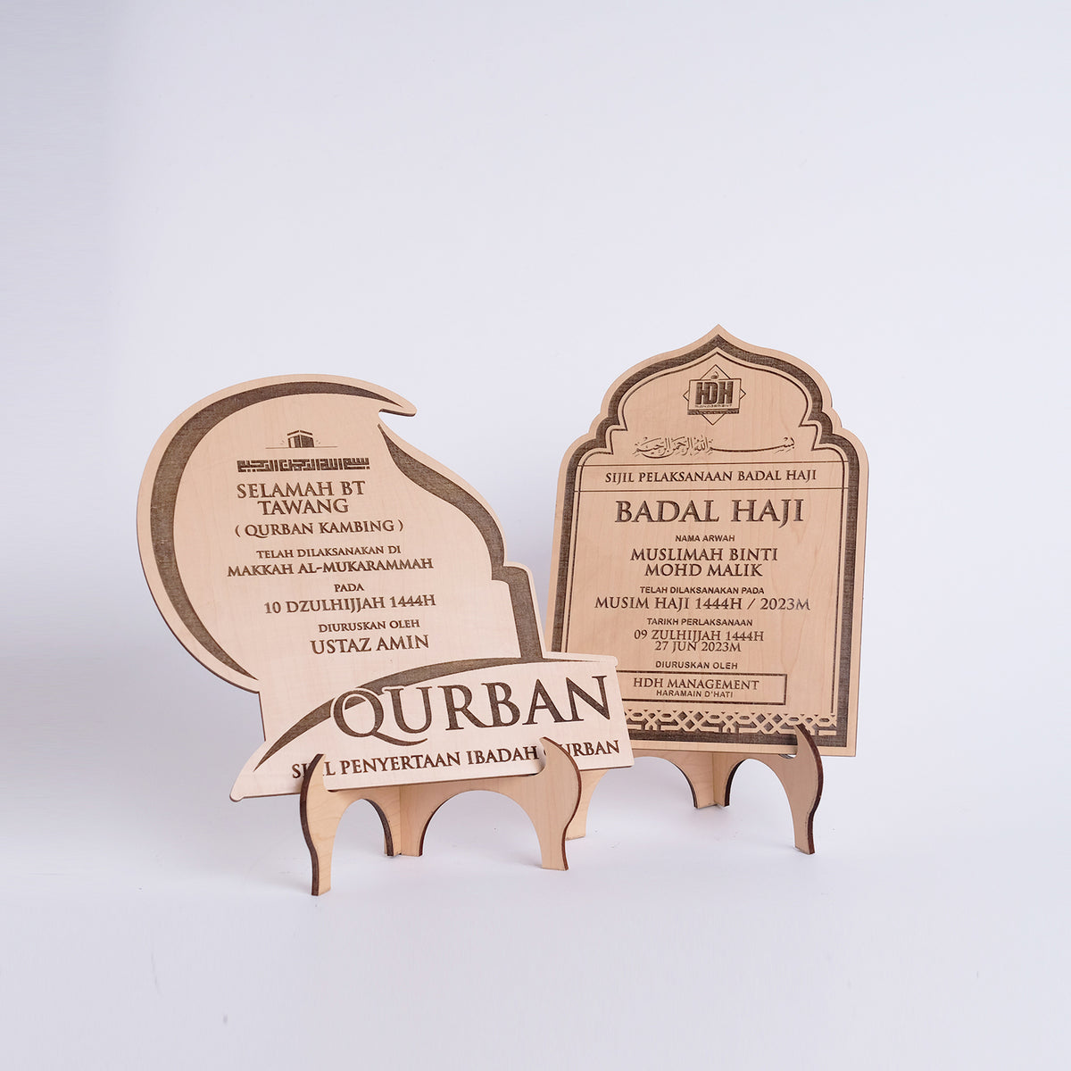 Two wooden Qurban certificates on a stand with engraved text on a white background