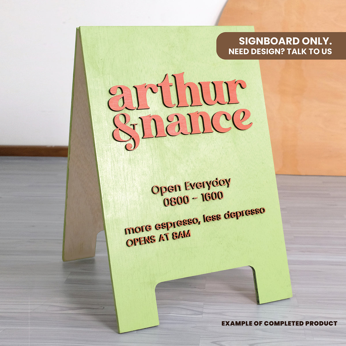 Green signboard with red text displaying 'Arthur & Nanice' and opening hours on a wooden surface.
