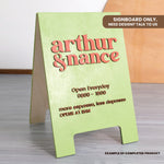 Green signboard with red text displaying 'Arthur & Nanice' and opening hours on a wooden surface.
