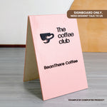 Pink signboard with 'The Coffee Club' and 'BeanThere Coffee' text on a wooden surface.