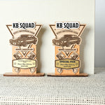 Two wooden trophy-like awards with 'KB Squad' branding on a textured surface.