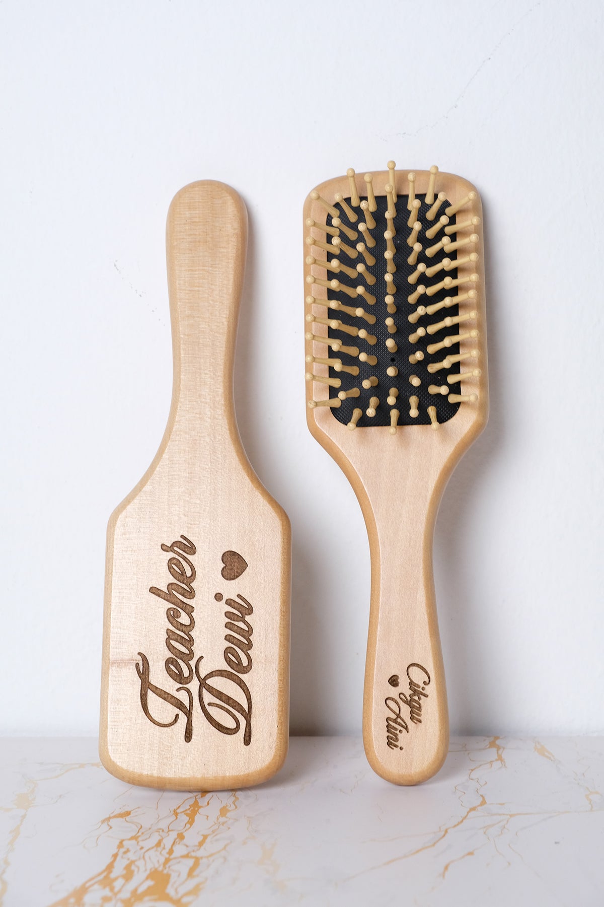 Two wooden hairbrushes with engraved text on a light background