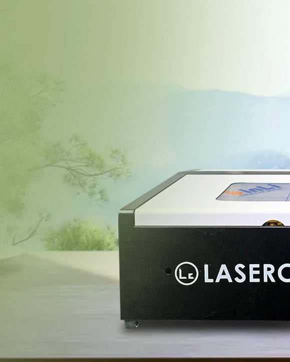 Laser cutting machine with 'LASERCUT.MY' branding on a desk with a scenic background.