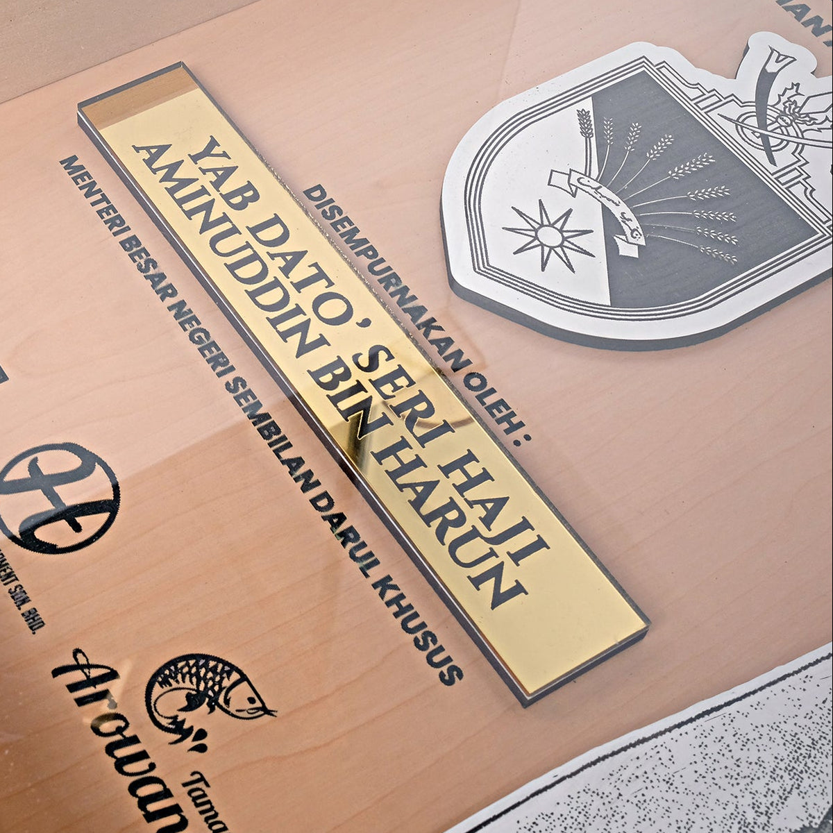 Wooden plaque with engraved text and logos, framed by a black border.