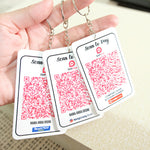 Three keychain cards with QR codes and branding held by a hand.